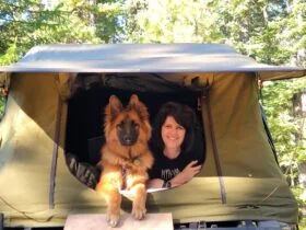 Woman and her German Shepherd dog laying at the entrance of a tent looking at the camera.