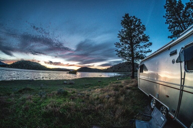 Airstream trailer parked in front of a lake with a sunset in the background.