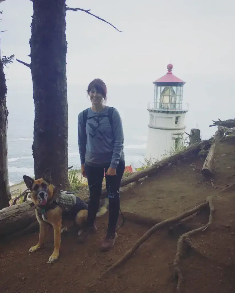 Woman and German Shepherd Dog on a hike standing in front of a lighthouse.