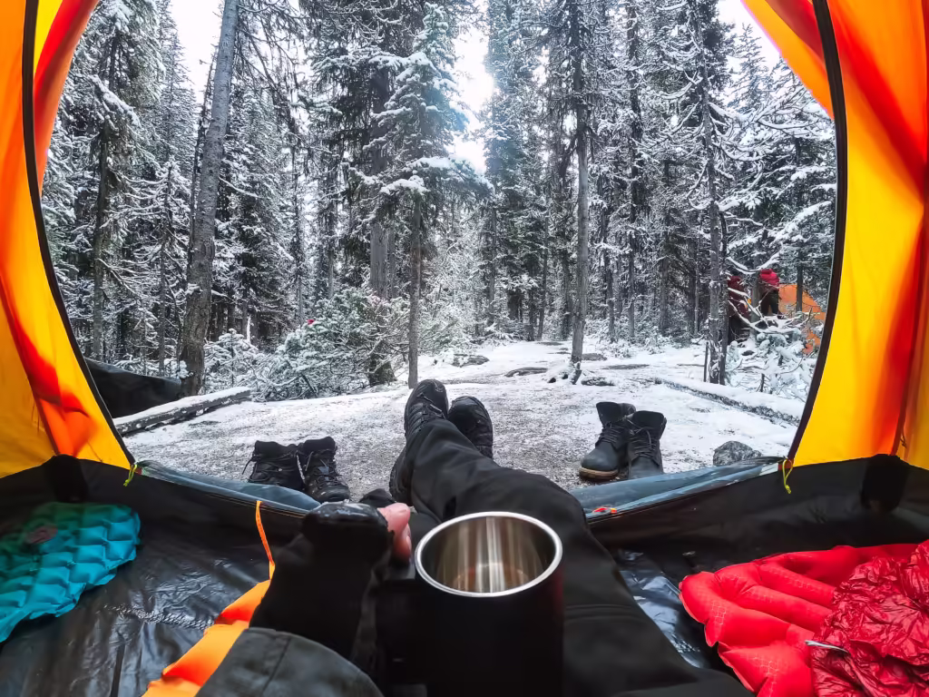 Traveler camping with hand holding cup in a tent with snow in pine forest at national park.