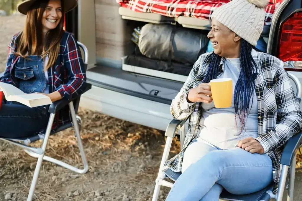 Multiracial women friends having fun camping with camper van while drinking coffee outdoor.