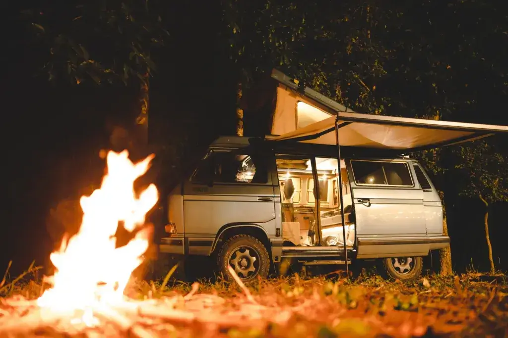 Camper van with an awning next to a camp fire.
