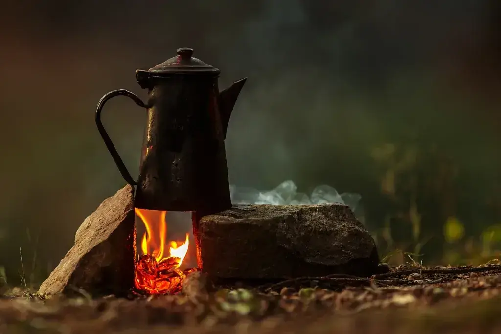 Coffee is brewed on a small fire in a rustic red camping kettle.