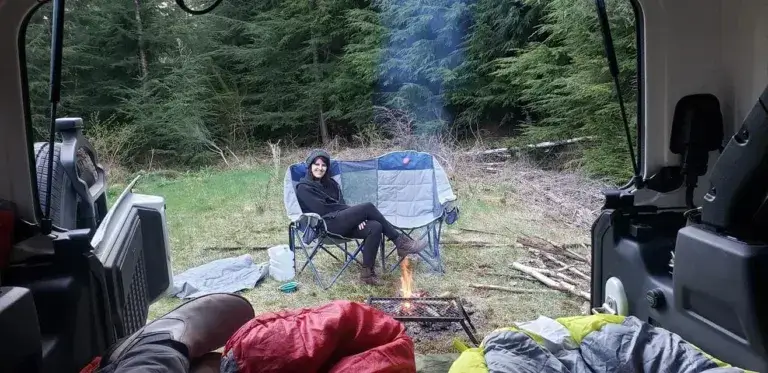 Woman sitting on a camp chair next to a camp fire looking into a Jeep Wrangler.
