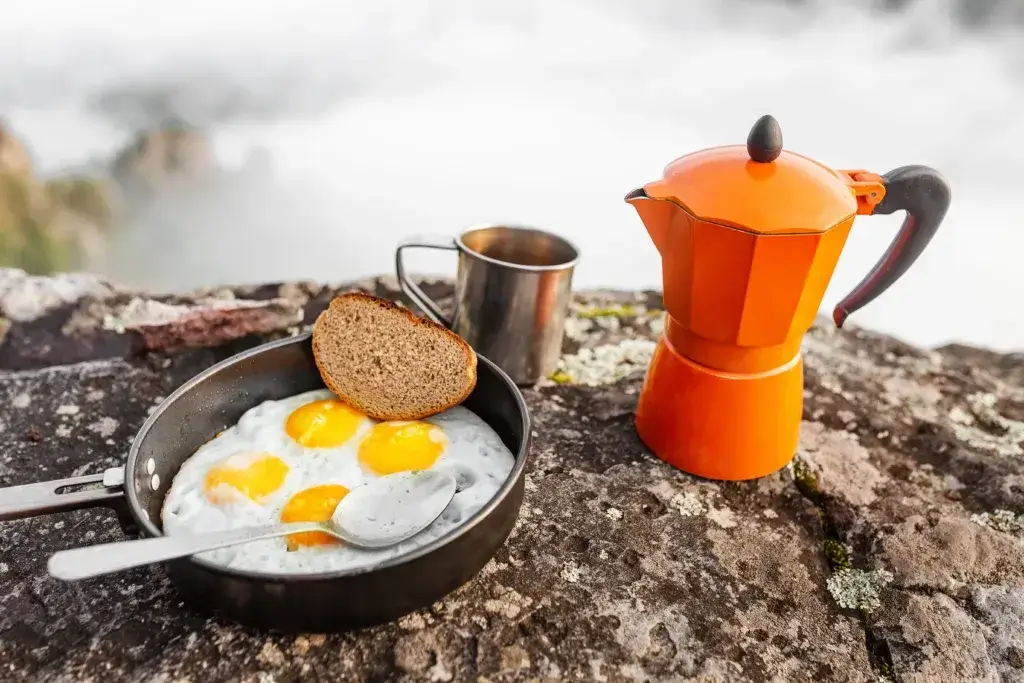 Fried eggs in a pan and coffee geyser maker outdoors in the mountains.
