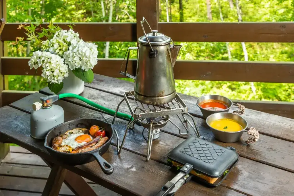 Table with a propane tank and stove boiling a kettle, and breakfast food.