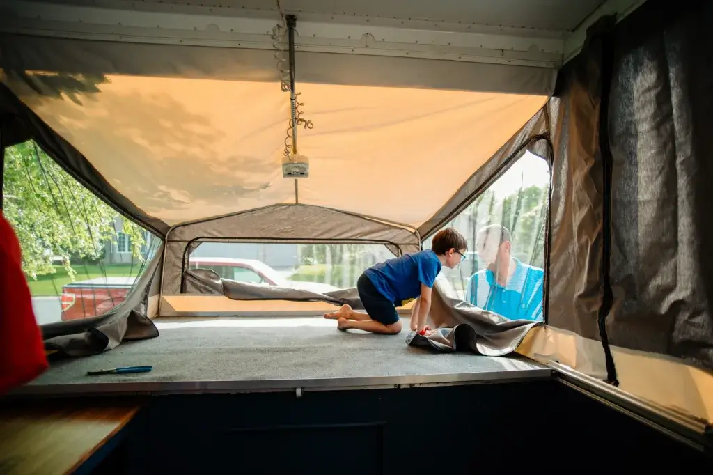 Bed in popup camper with a child looking out the window.