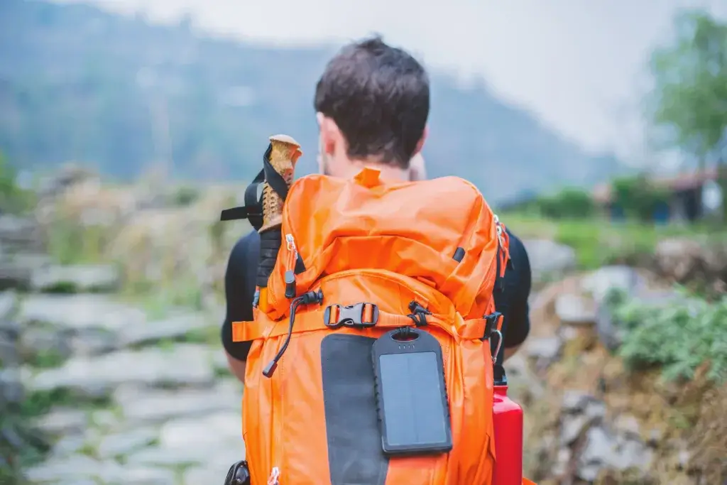 Kid hiking with an orange backpack and solar charger hooked on the back.