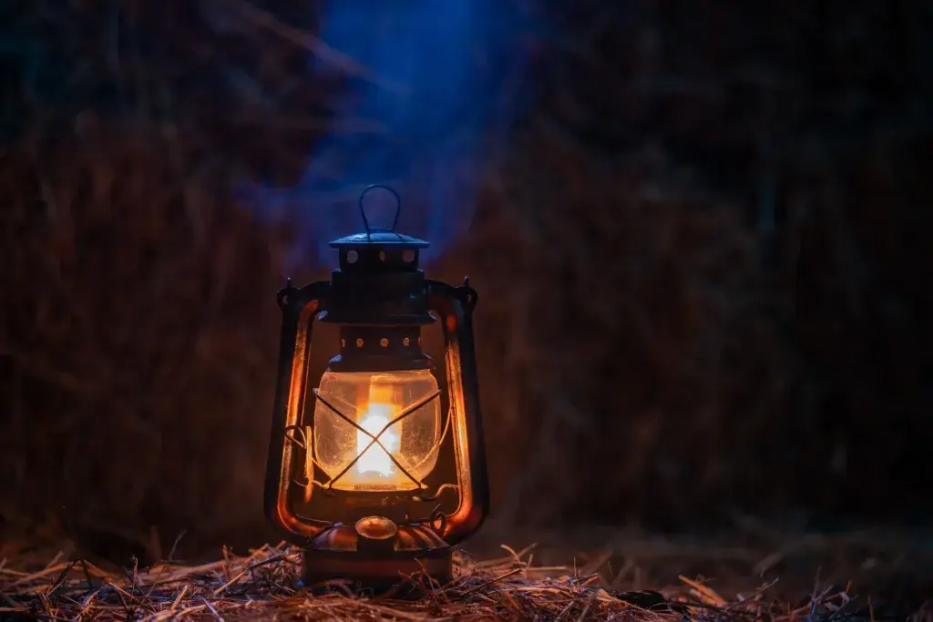 Lantern is sitting on a table at camp at night.