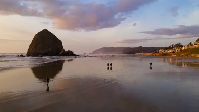 People walk on the beach reflection late afternoon at dusk in Cannon Beach Oregon.