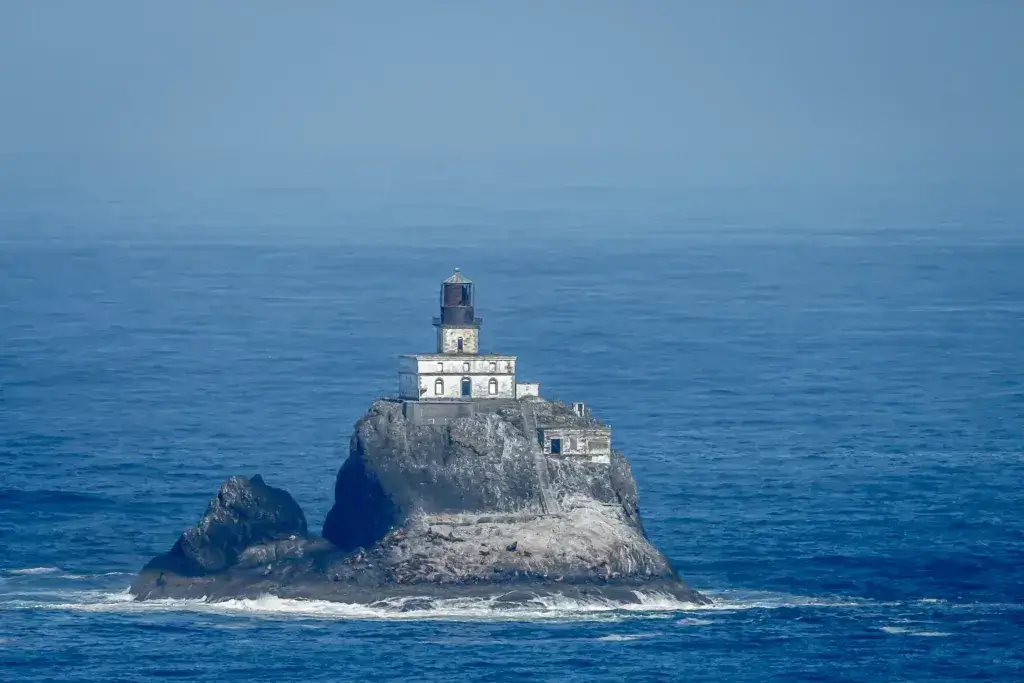 Tillamook lighthouse against a blue ocean with sealions on the rocks.