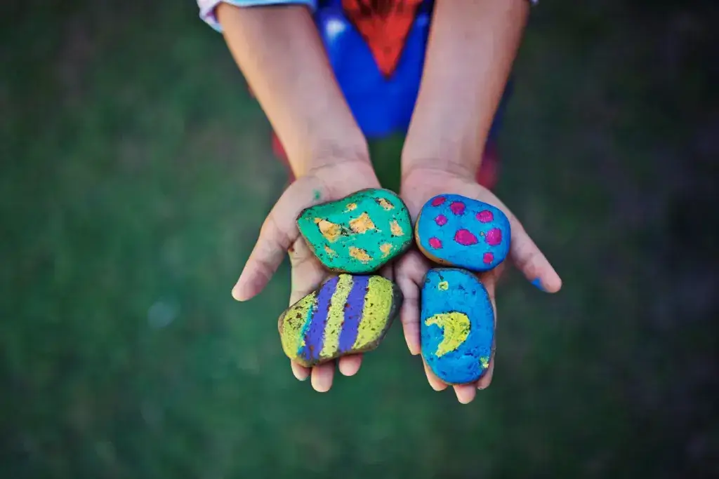 Child showing camping crafts, painted stones.