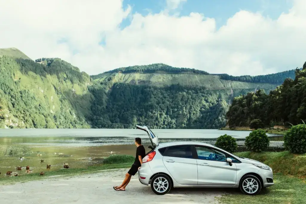 Young man sitting in his car trunk and resting while enjoy the beauty of natural lake.