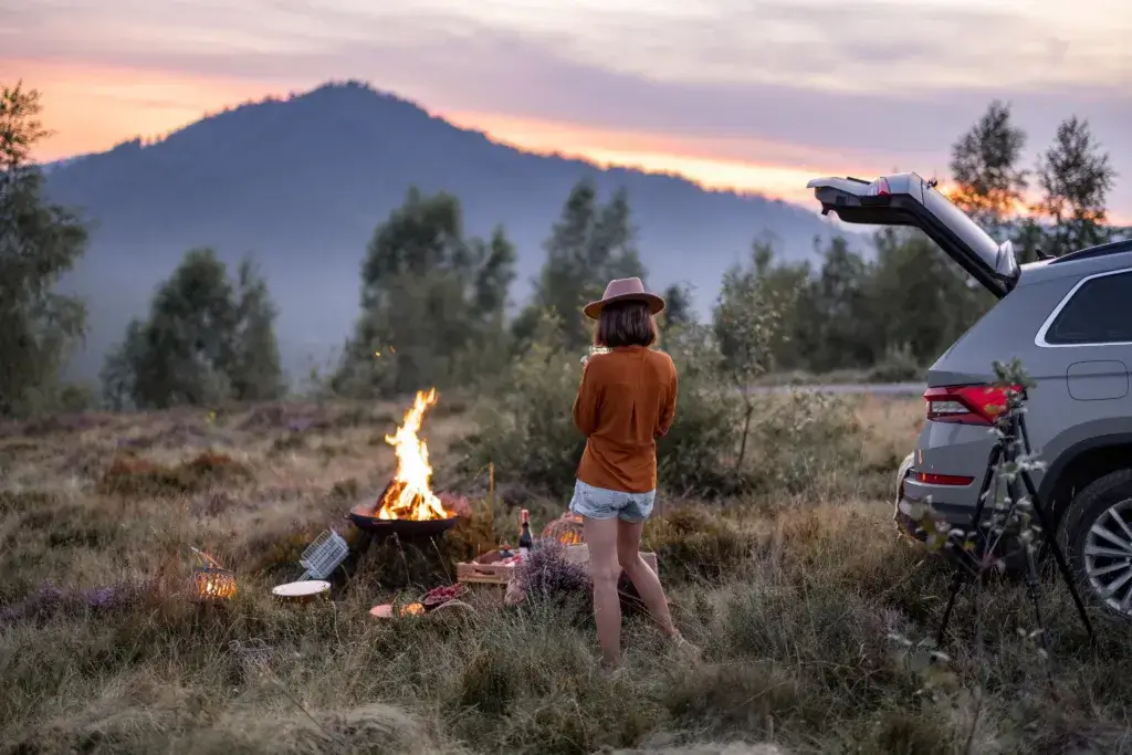 Woman photographing a bonfire on phone, having a beautiful picnic in the mountains. Travel by car, use of mobile devices in nature.
