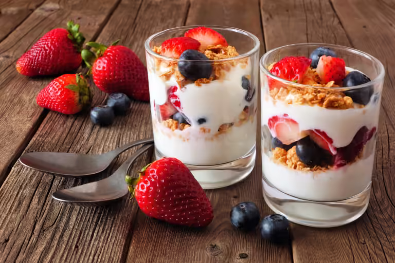 Strawberry and blueberry parfaits in glasses against a rustic dark wood background.