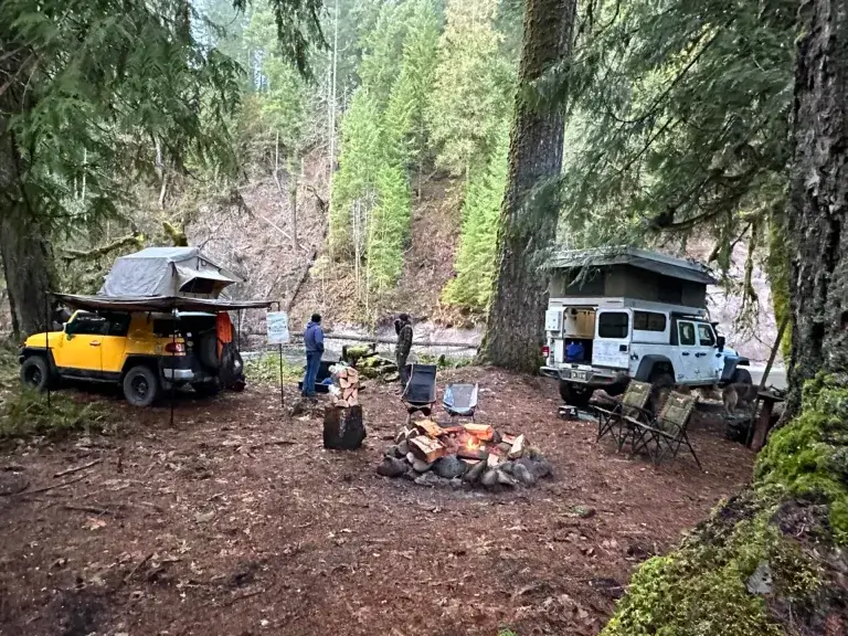 Two vehicles with rooftop tents at a river side camp site.