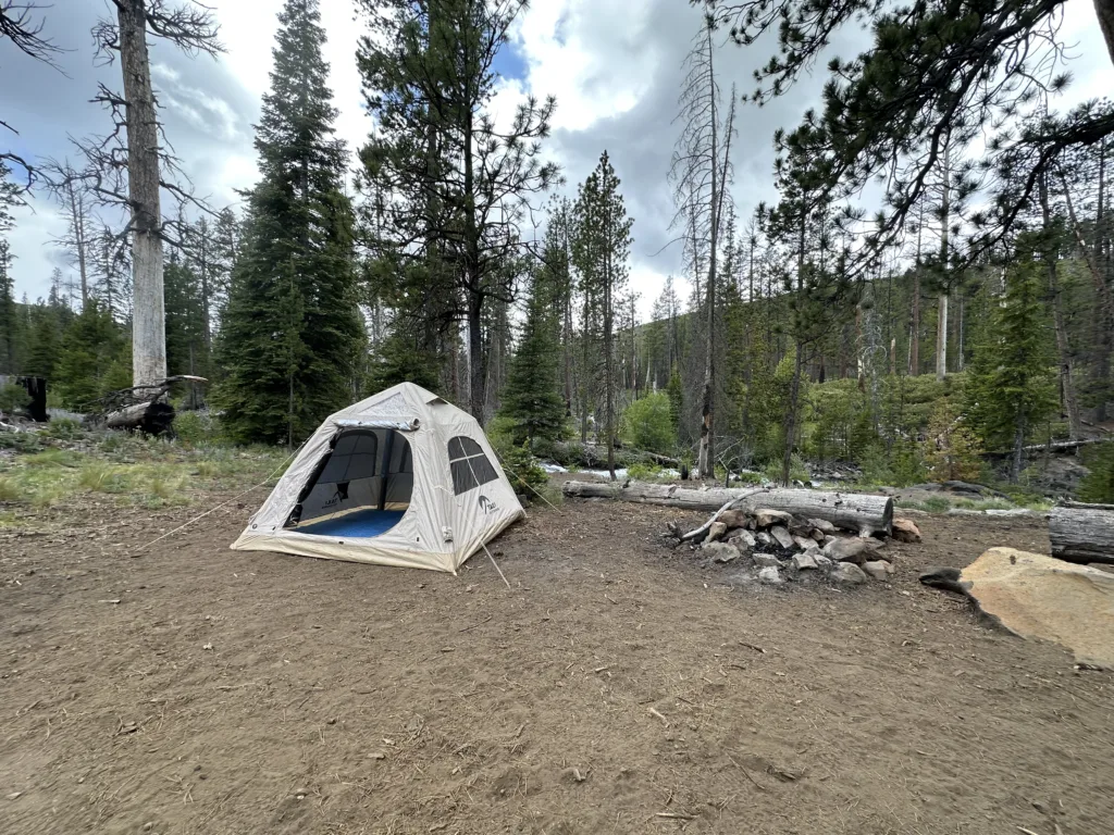 Tebnt camping in the wilderness with a rock fire pit and stream in the distance.