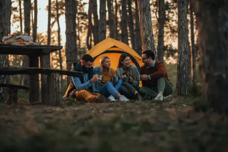 Four young friends sitting outside their tent drinking hot beverages and socializing.