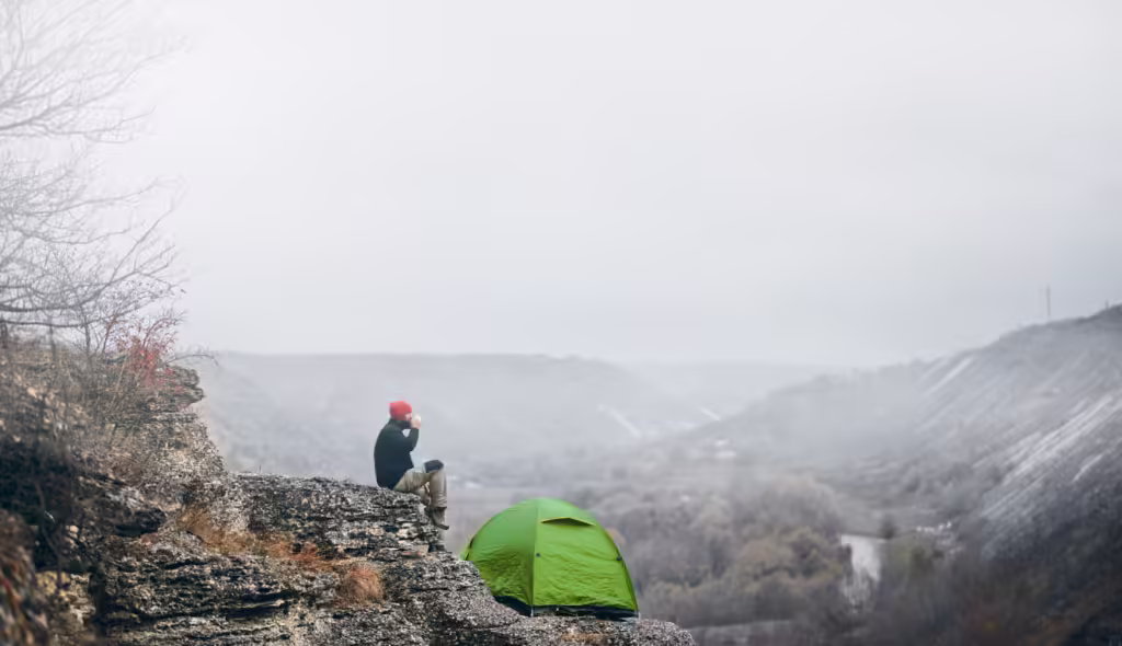 Landscape view of a man traveler relaxing in mountains near of tent camping gear outdoor.