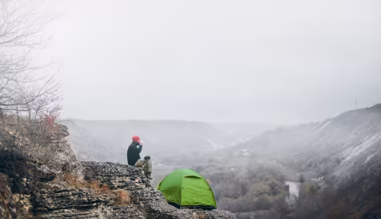 Landscape view of a man traveler relaxing in mountains near of tent camping gear outdoor.