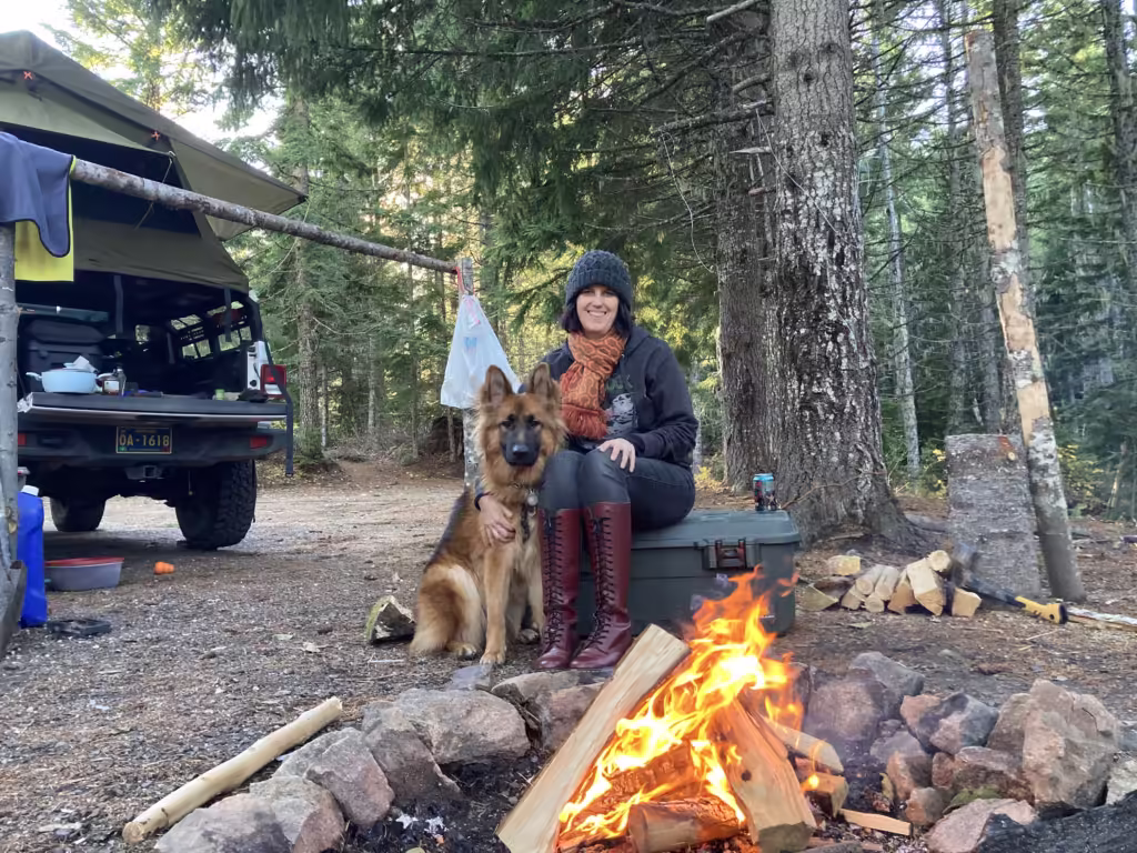 Woman and German Shepherd dog sitting next to a campfire while car camping.