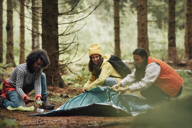 Smiling group of diverse female friends setting up their campsite after a day hiking together in the woods.