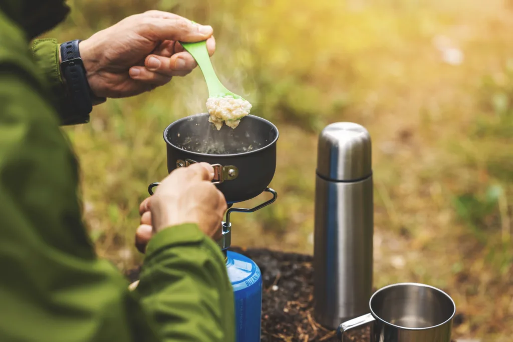preparing oatmeal porridge outdoors on gas burner.