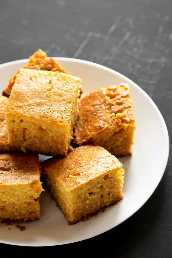 Cornbread cut into squares on a white plate.