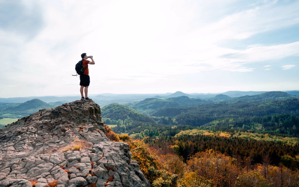 Man standing on a mountain peak stopping to take a drink of water on a hike.