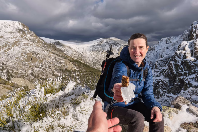 Woman on a snowy hike handing a granola bar to a fellow hiker.