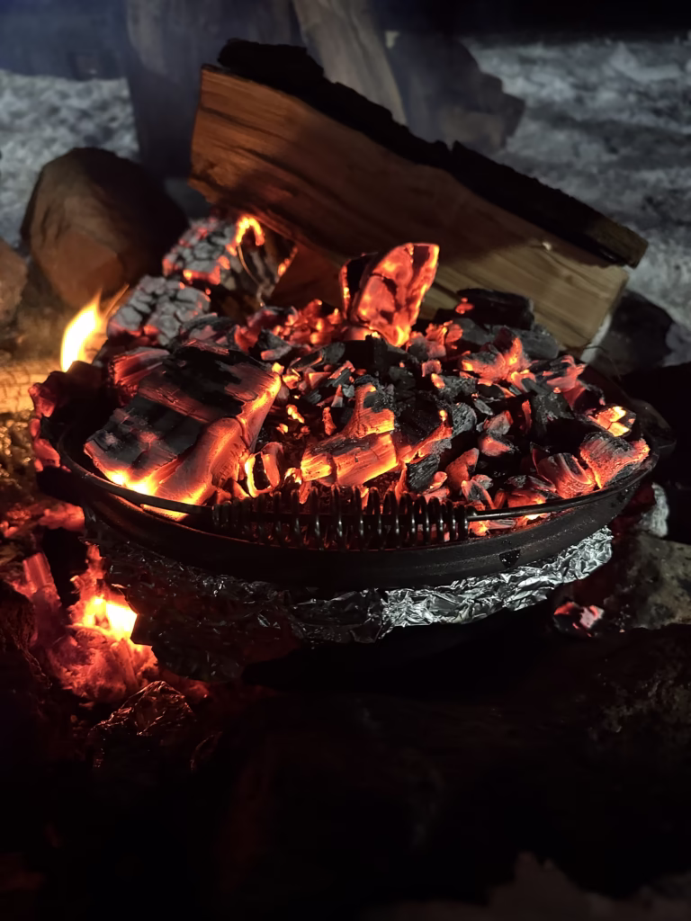Dutch oven sitting on campfire with coals on top of lid.