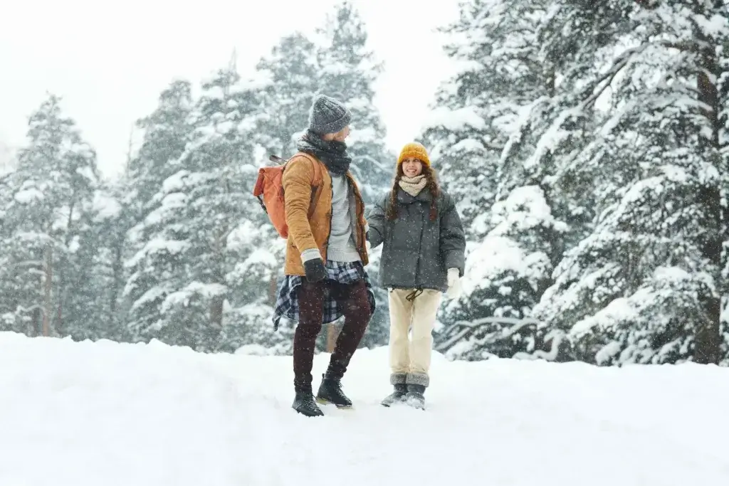 Man and woman hiking in the snow with snowy pines in the background.