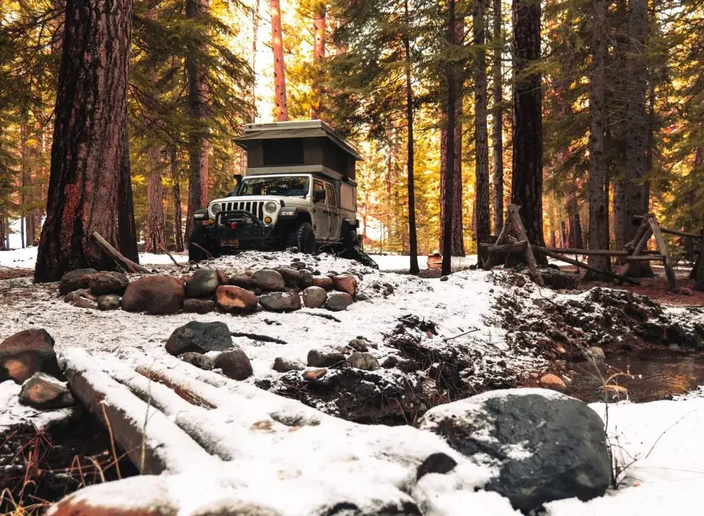 Jeep Gladiator with a popup tent in a snowy forest setting.