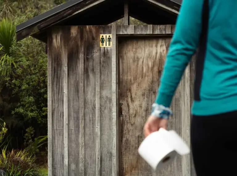 Person with toilet paper in hand heading to pit vault toilet at campground.