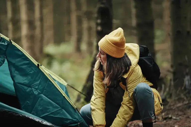 Young woman next to a tent solo camping in the forest.