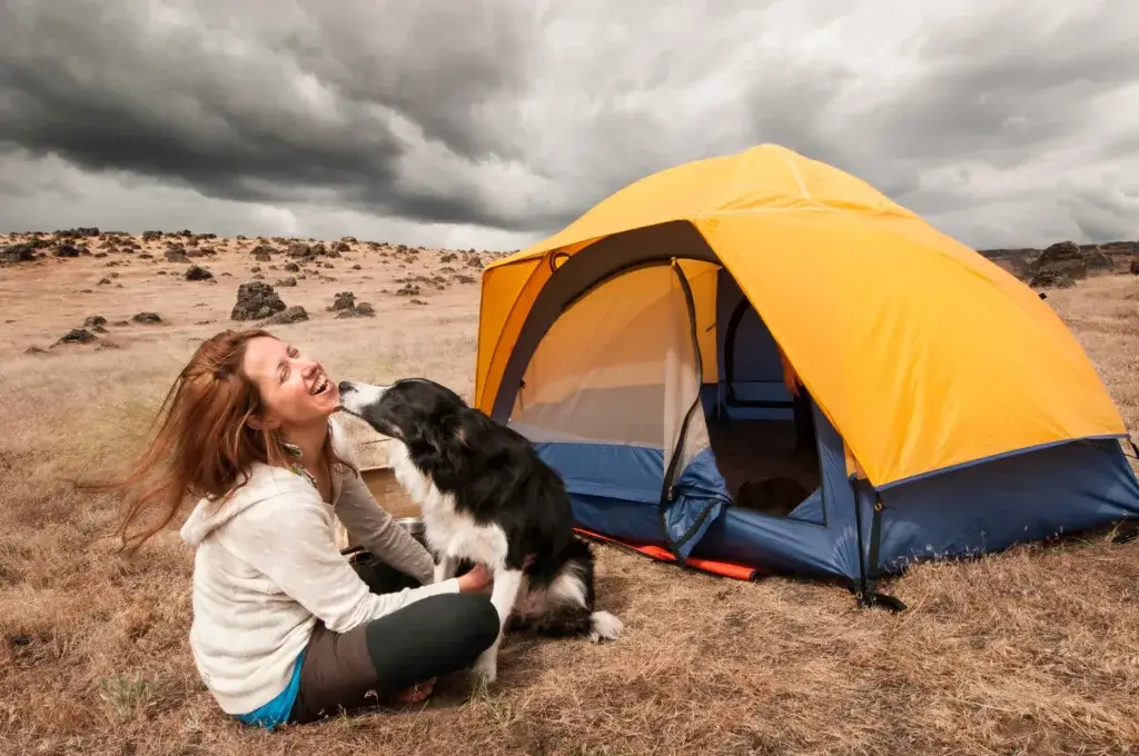 Woman and dog sitting next to a tent with a storm looming in the background,