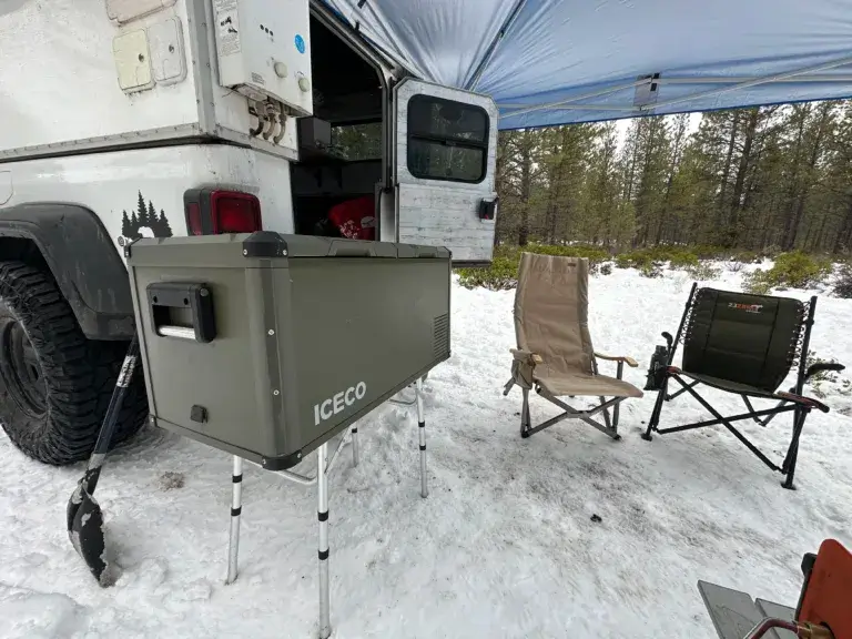 Iceco refrigerator green refrigerator sitting on a table at camp with a snowy background.