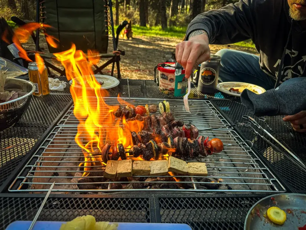 Friends grilling kebabs over flames on the AroundFire portable fire pit.