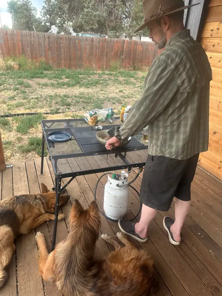 Man cooking hamburgers on the porch using the Around Fire camping stove.