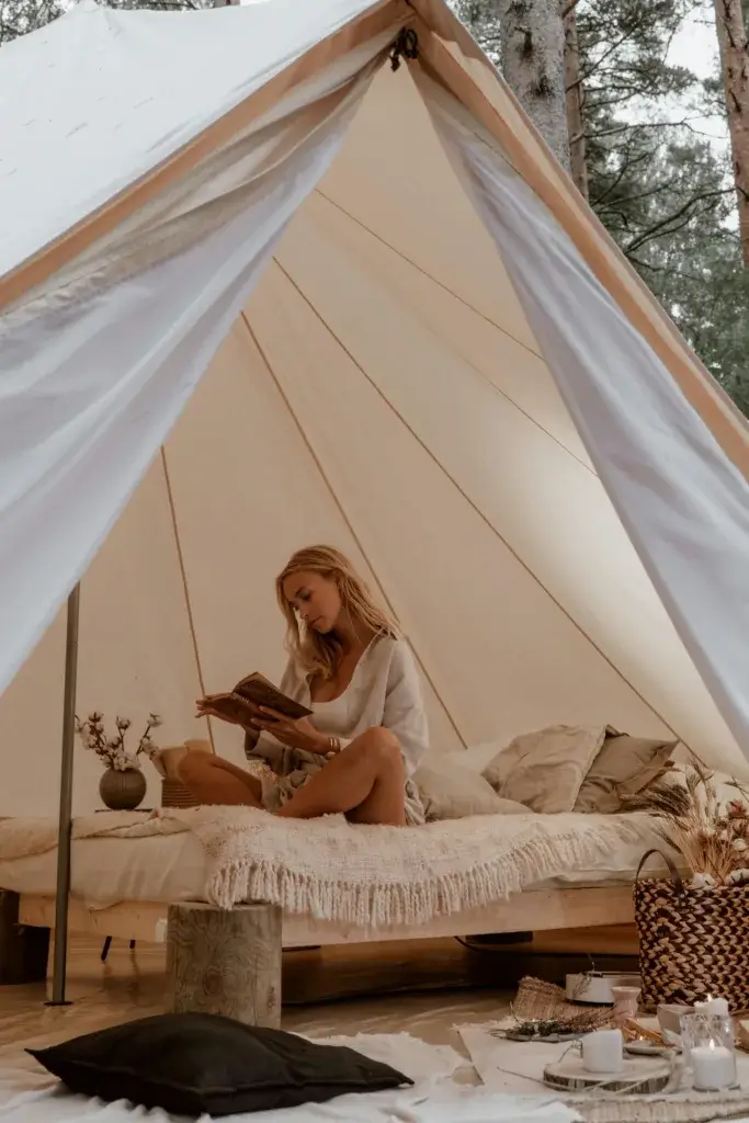A woman relaxes while reading inside a comfortable glamping tent.
