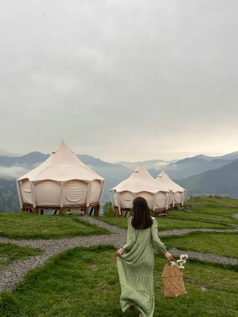 Woman in green dress walking towards tents in the Georgian mountains.