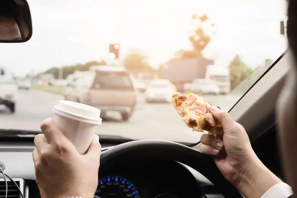 Person holding a coffee and snack while driving on a roadtrip.