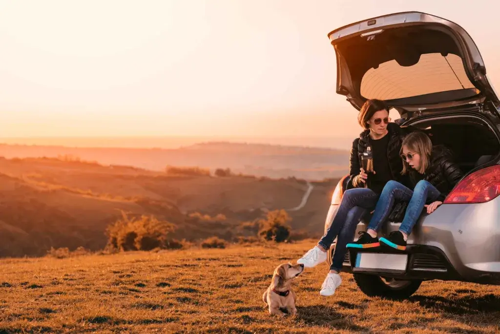 Young mother and child sitting in the trunk of a car admiring the view on a roadtrip.