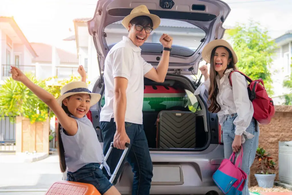 Family packing excitedly loading suit cases into a car for a roadtrip.