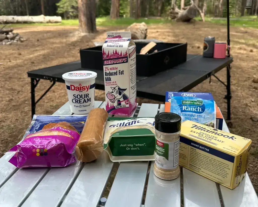 Ingredients for Ranch Mac N Cheese sitting on a table at a campsite.