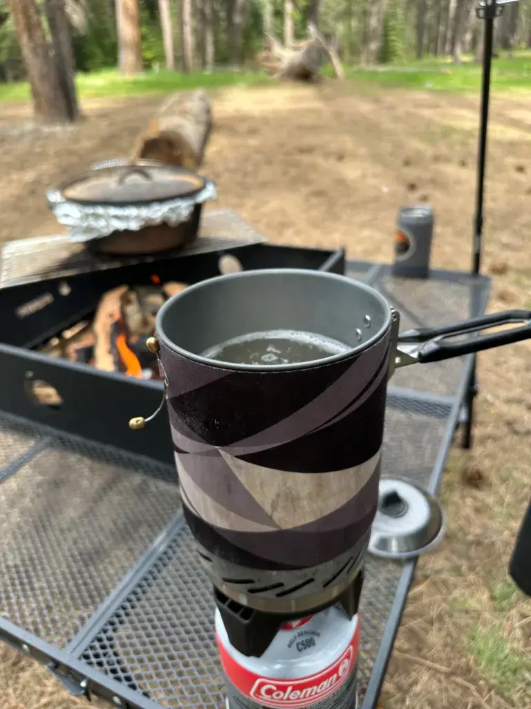 Boiling noodles in a Jet Boil at camp with a Dutch Oven in the background.
