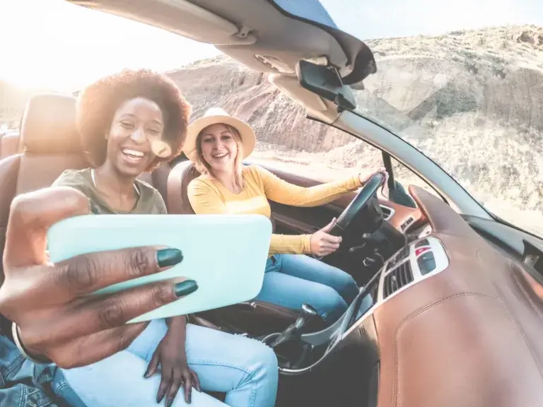 Happy girls having fun in convertible car in summer vacation - Young women friends taking selfie on cabriolet auto outdoor - Main focus on blond girl face - Travel, holidays and friendship concept