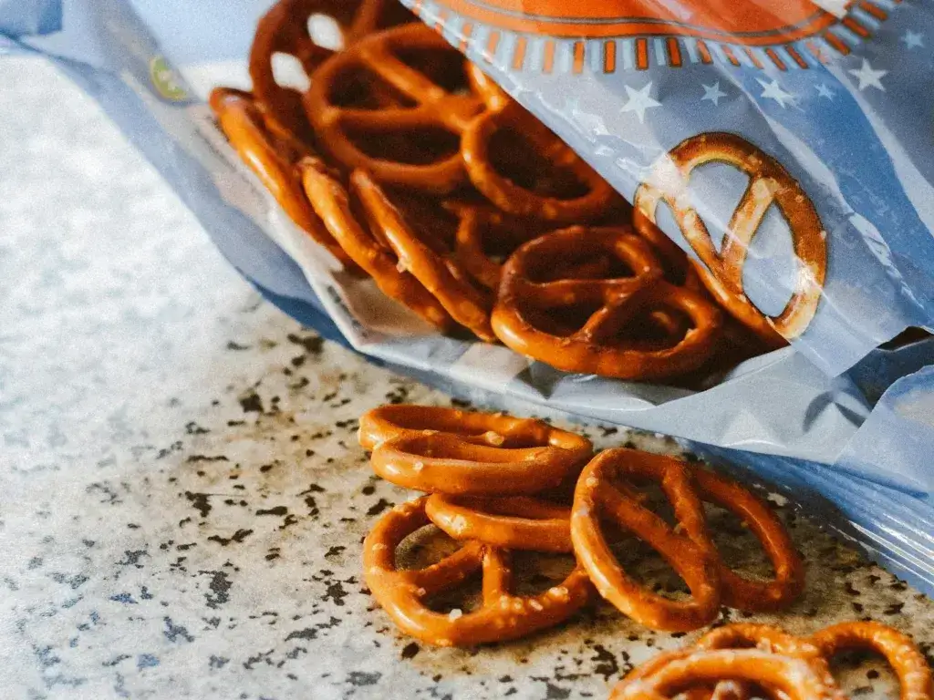 Crispy salted pretzels spilling from an open snack bag on a textured surface.