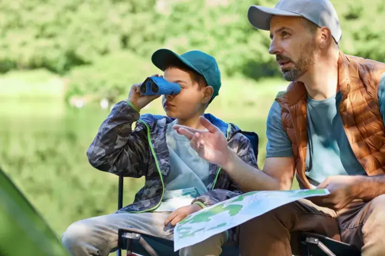 Father and son with a map and binoculars on a scavenger hunt in nature.