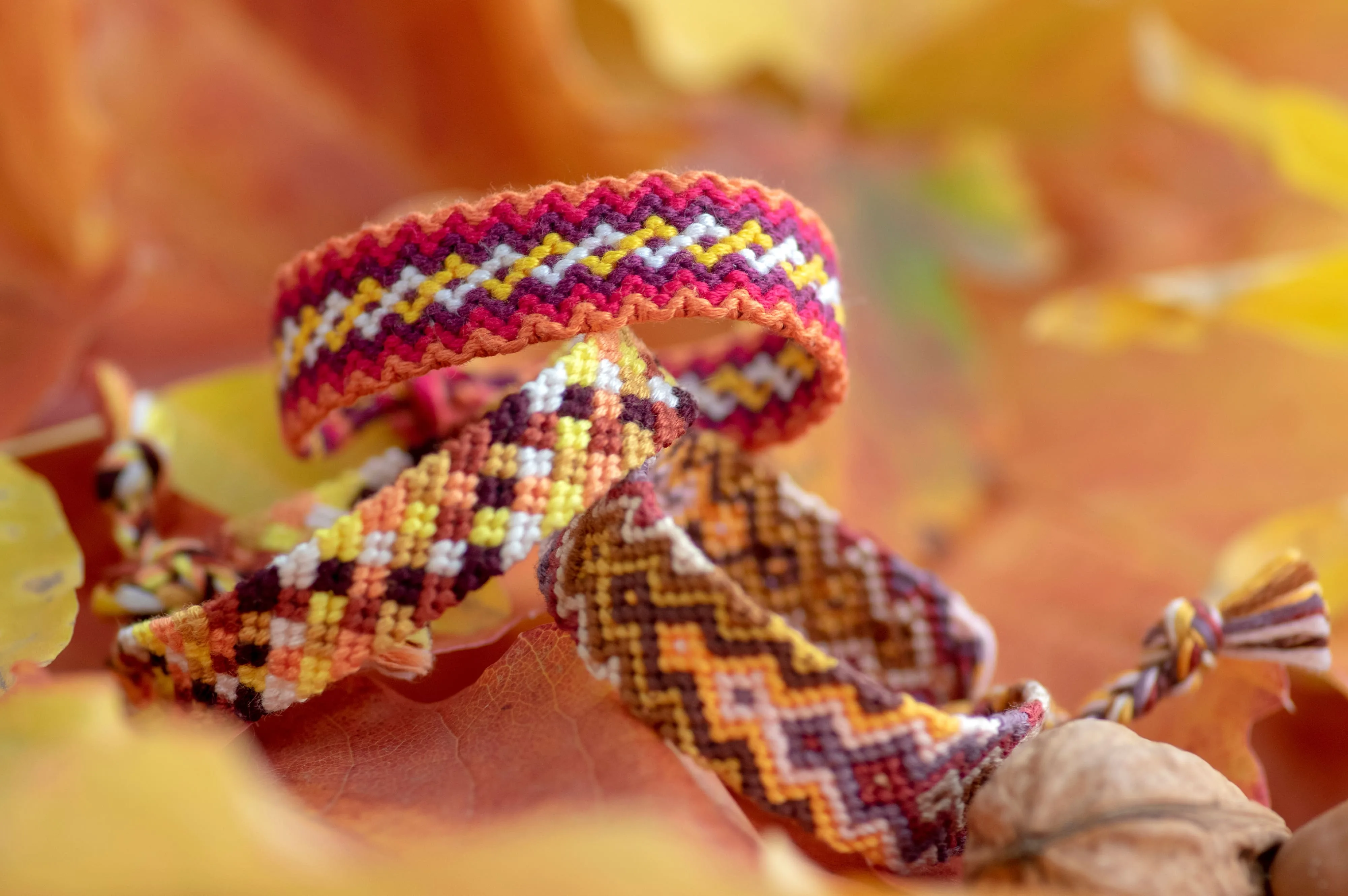 Three handmade friendship bracelets sitting on fall leaves.